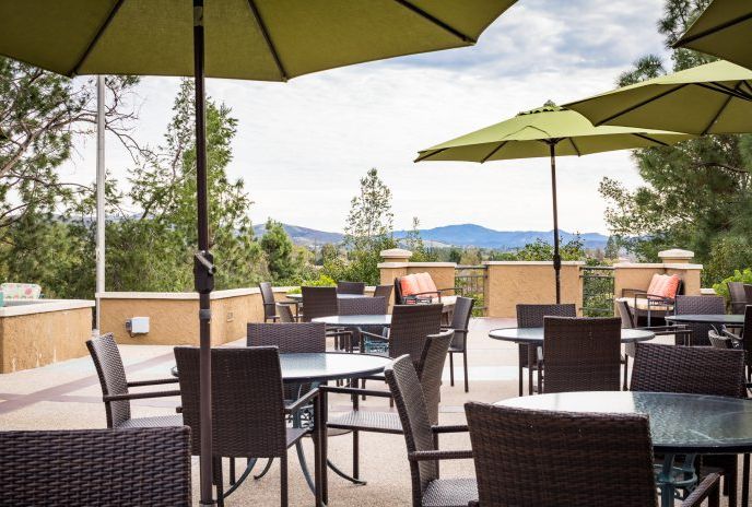 A scenic outdoor patio with tables, chairs, and green umbrellas overlooking a mountainous landscape.