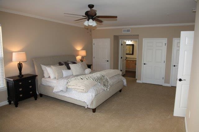 A cozy and spacious bedroom with a neatly made bed, carpeted floor, and a ceiling fan.