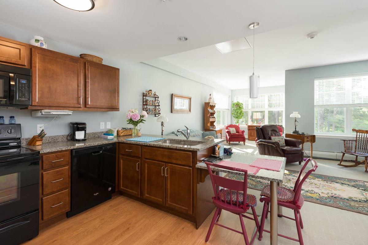 Open floor plan featuring a kitchen with wooden cabinets, dining table, and a living room with ample natural light.