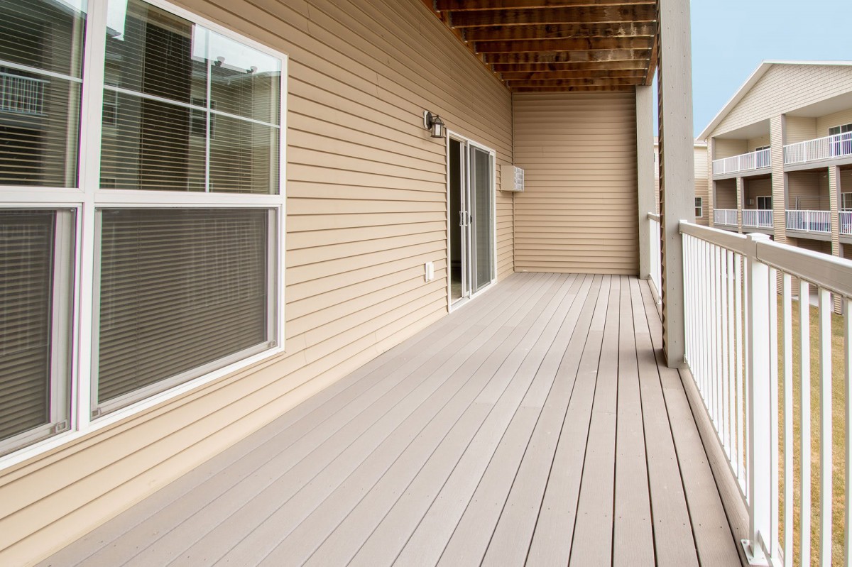 A spacious wooden balcony with a sliding door and window, featuring a railing for safety.