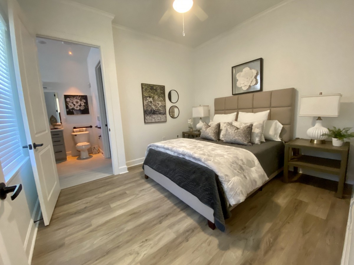 A modern bedroom featuring a stylish bed with plush pillows, elegant artwork, and wooden flooring.
