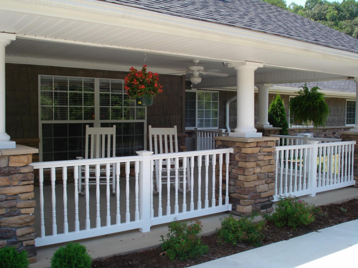 A cozy front porch with rocking chairs and white railing, featuring hanging plants and stone pillars.
