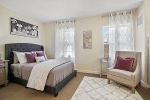 A cozy bedroom with elegant decor, featuring a bed, chair, and natural light from the windows.