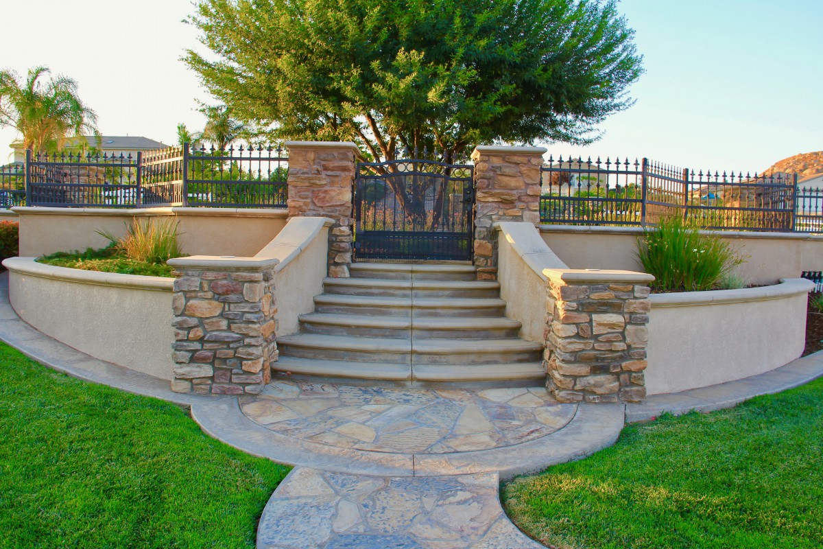 A landscaped garden entrance with stone stairs leading up to a wrought iron gate.