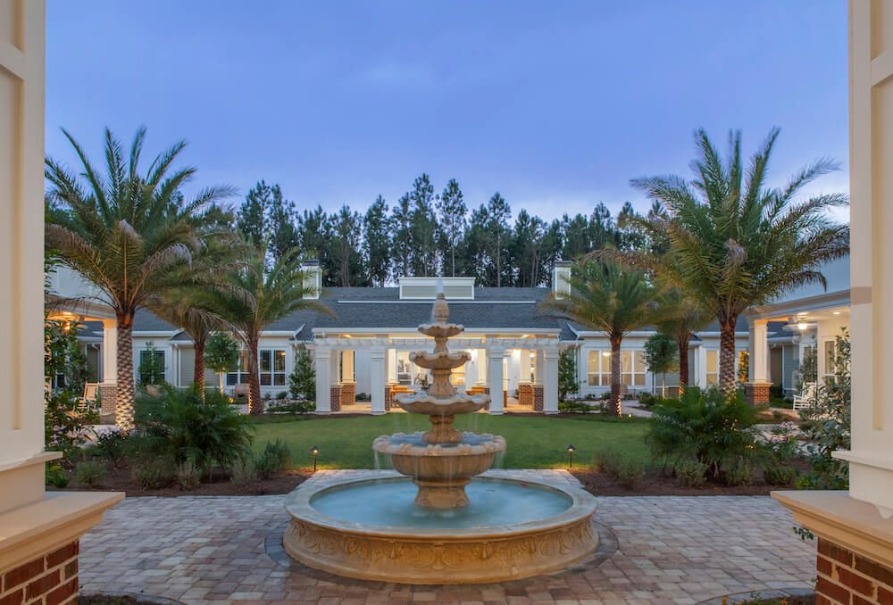 A luxurious mansion with a grand fountain surrounded by palm trees during the evening.