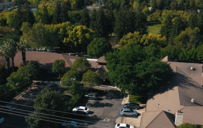 Aerial view of a suburban area with buildings, a parking lot, and surrounding trees.