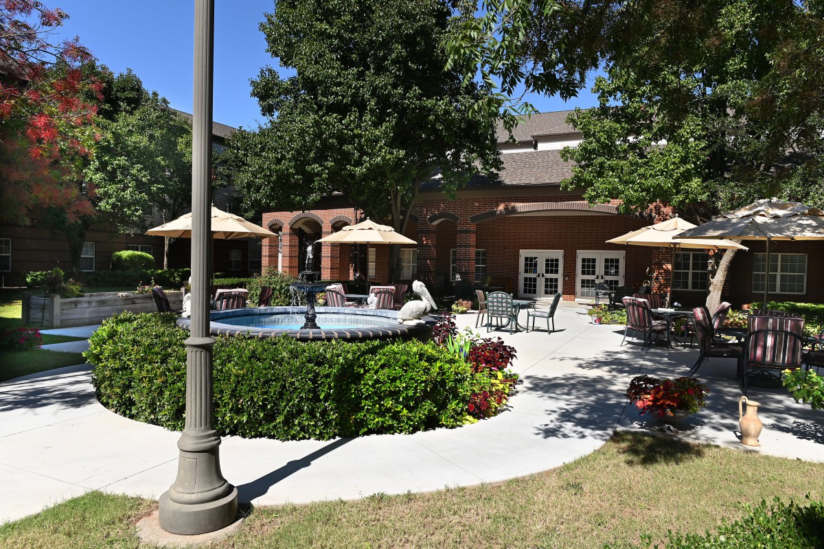 A sunny outdoor patio area featuring a fountain, surrounded by tables and umbrellas amidst lush landscaping.
