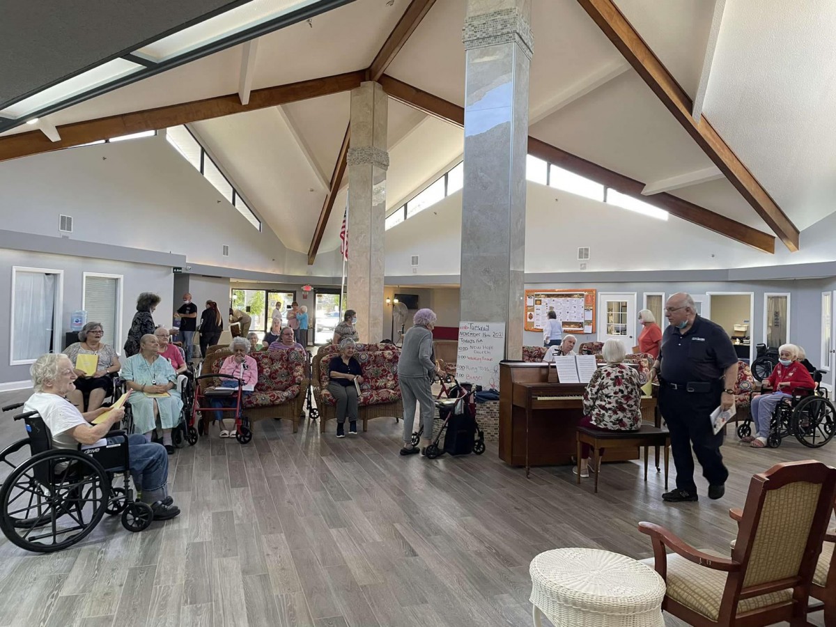 A community center with seniors gathered for an event, some using wheelchairs and others standing or sitting, during the daytime.