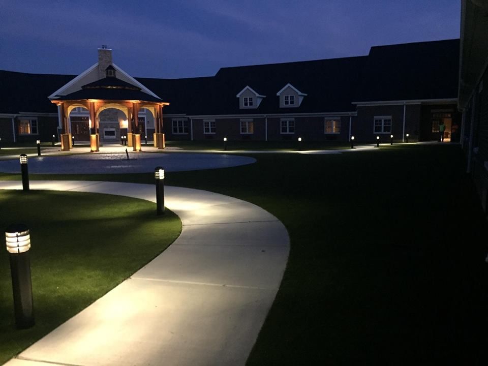 A well-lit pathway leading to a building and pavilion at night.