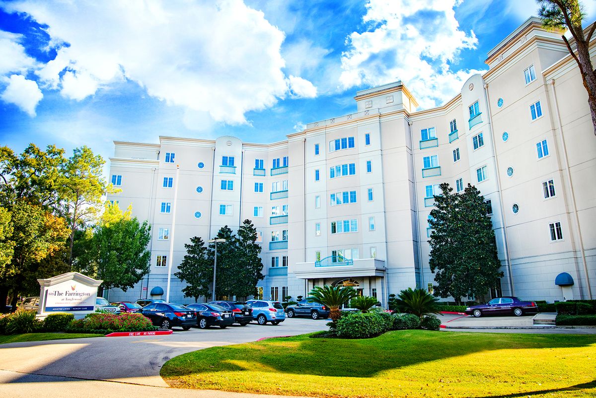 A residential apartment building with a parking lot and landscaped gardens under a partly cloudy sky.