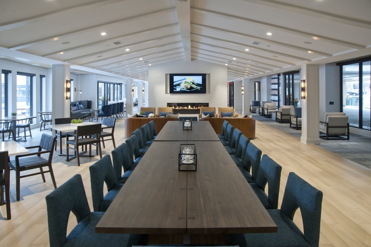 A modern conference room with a long table and chairs, featuring a screen on the wall.