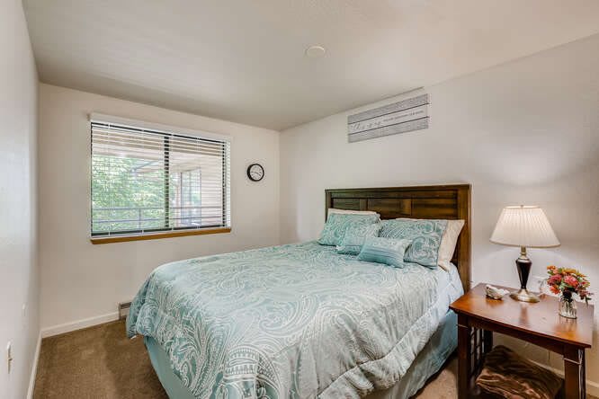 A cozy bedroom with a neatly made bed, a window allowing natural light, and a small bedside lamp.