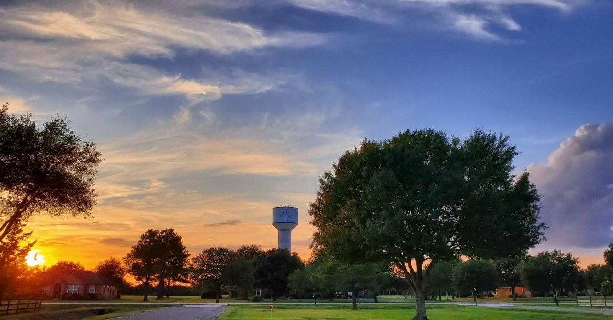 A picturesque sunset over a landscape with trees and a water tower.