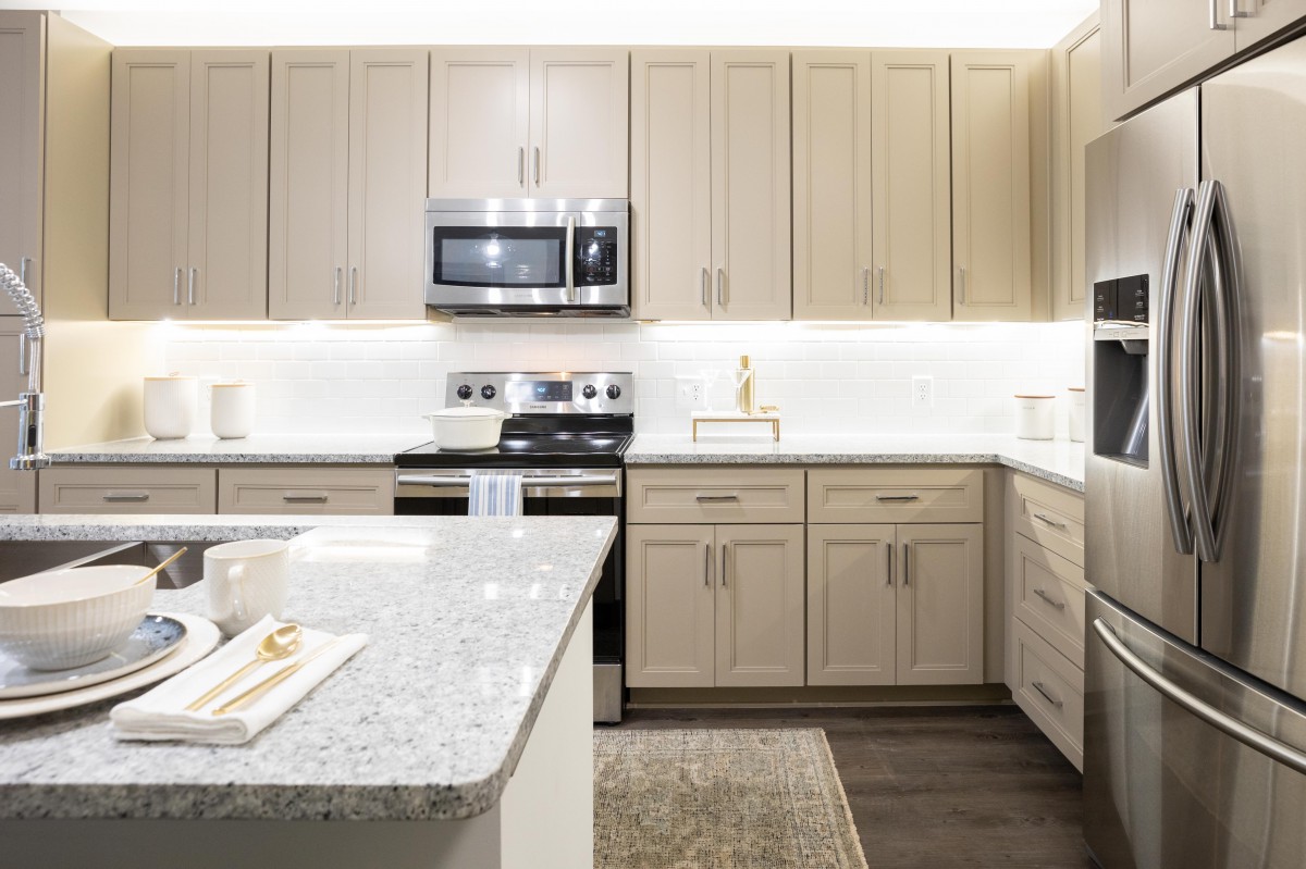 A modern kitchen featuring light wood cabinets, a granite countertop, and stainless steel appliances.