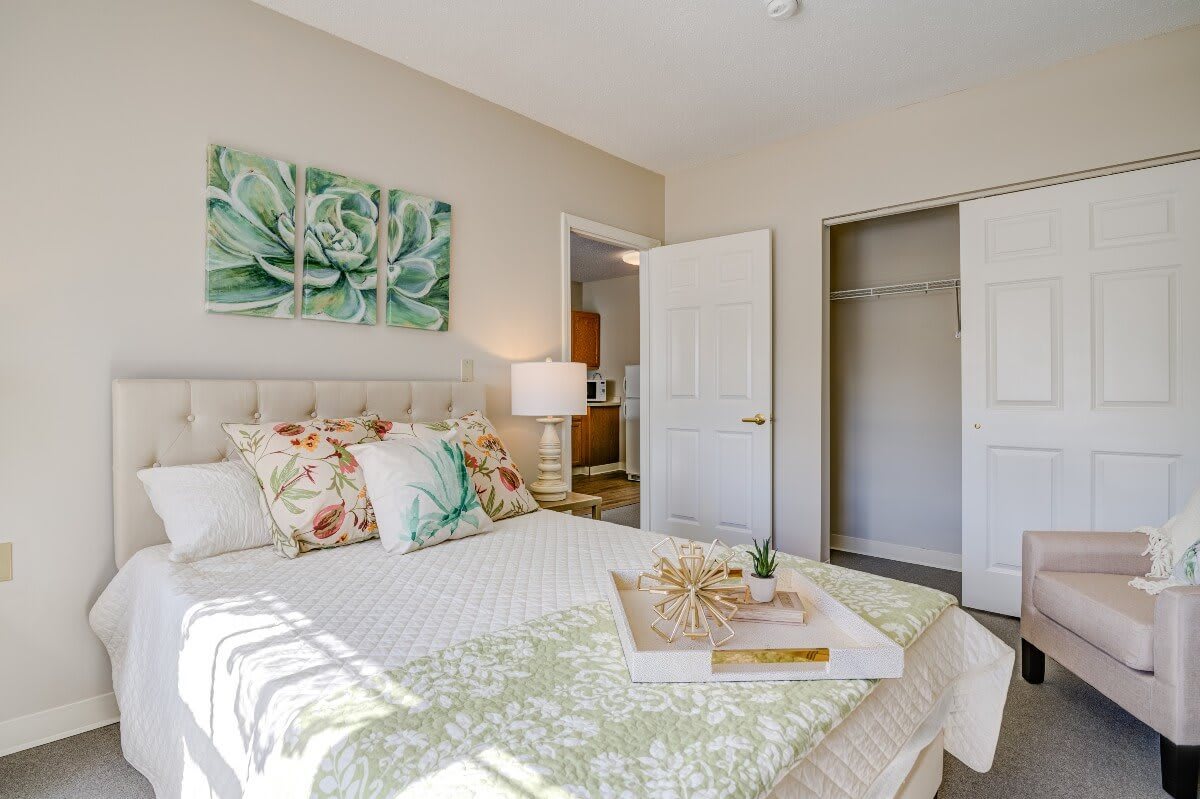 A bright and cozy bedroom with floral decor, featuring a neatly made bed, wall artwork, and an open closet.