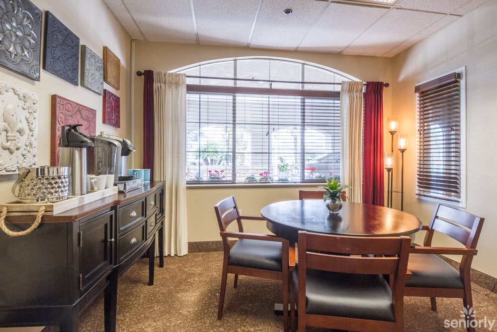 A well-lit office meeting room with a round table and chairs, featuring large windows and curtains.