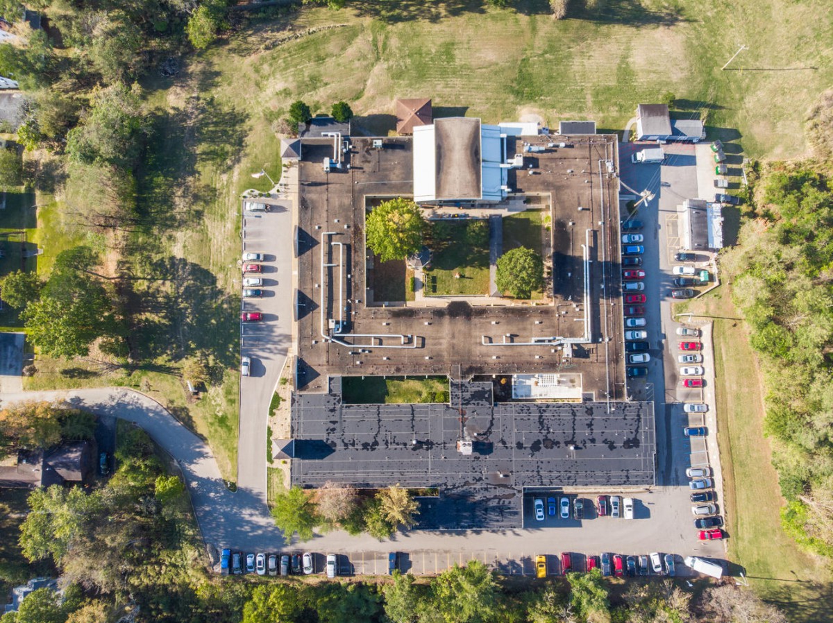 Aerial view of a building with surrounding greenery and a parking lot.