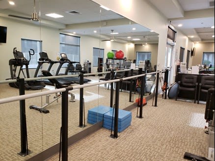 A spacious gym equipped with treadmills, balance bars, and aerobics mats in a well-lit environment.