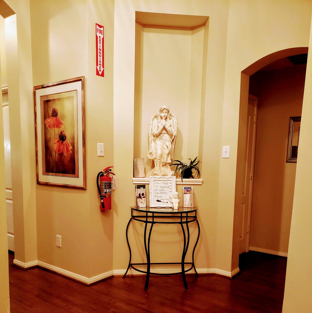A warmly lit hallway features a decorative statue, painting, and a fire extinguisher.