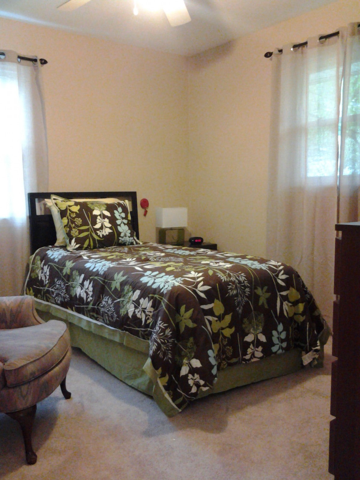 A cozy bedroom with a single bed featuring floral bedding, a chair, and a dresser.