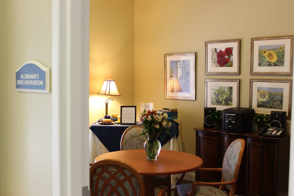 A cozy office space with a round table, chairs, decorative artwork, and a lamp on a side table.