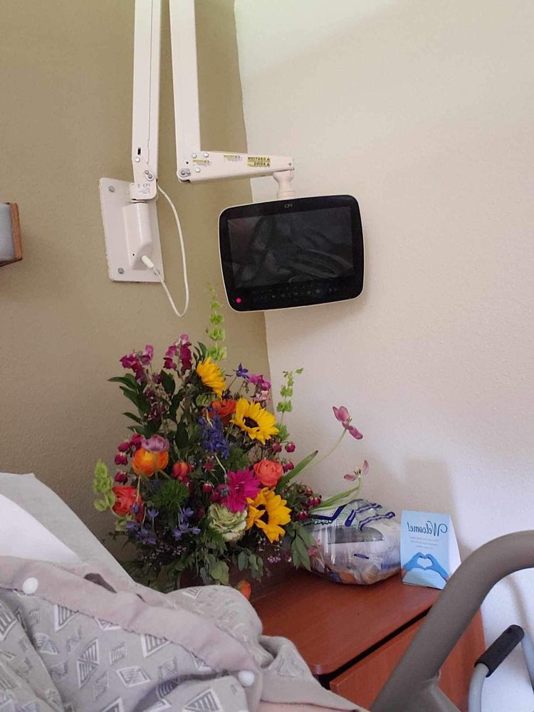 A hospital room with a bouquet of colorful flowers on the bedside table and a small TV mounted on the wall.