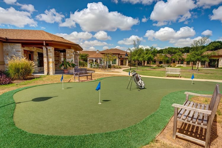 A scenic outdoor putting green surrounded by buildings under a partly cloudy sky.