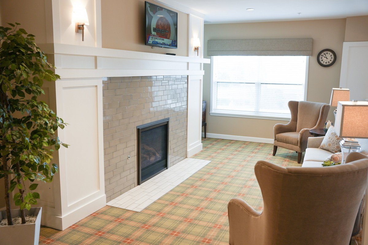 A cozy living room with a modern fireplace, armchairs, and a television mounted above the mantel.