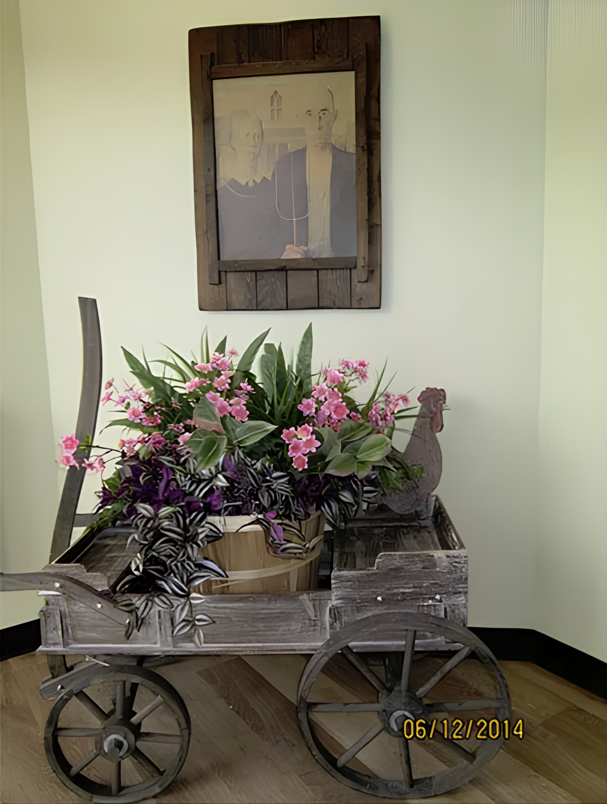 A decorative wooden cart with a vibrant flower arrangement, featuring pink and green hues, set against an indoor wall.