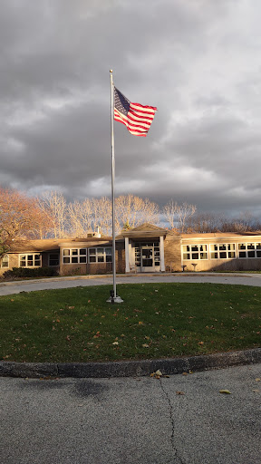 A school building with an American flag waving in front against a cloudy sky.