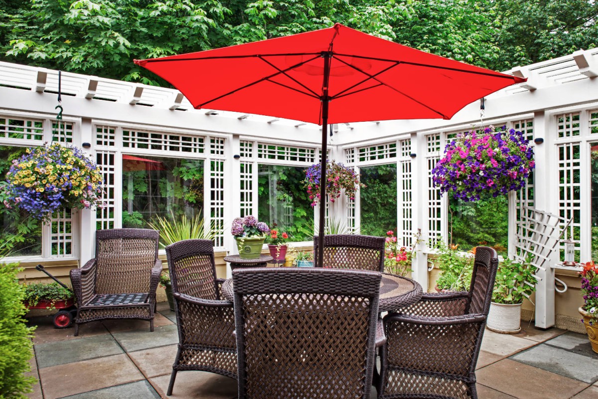 A charming outdoor patio with wicker chairs and a vibrant red umbrella.