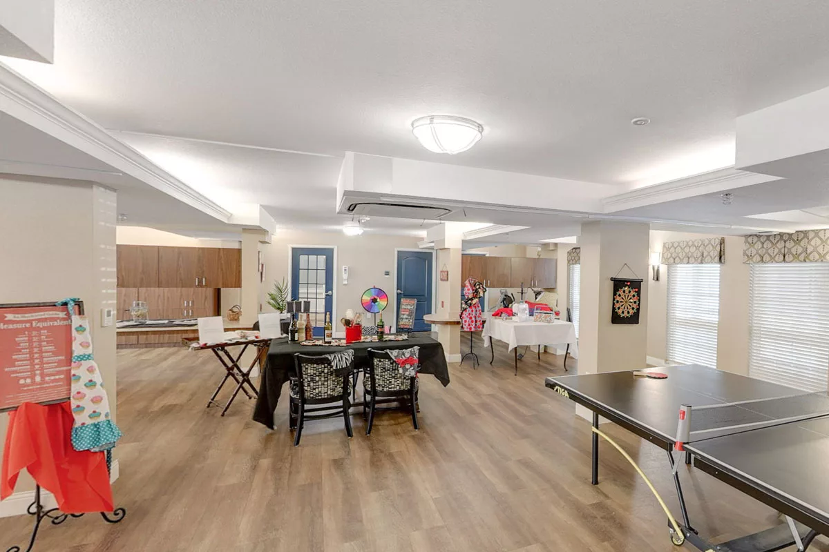 A spacious community room with modern furnishings, including tables, chairs, and wood flooring.