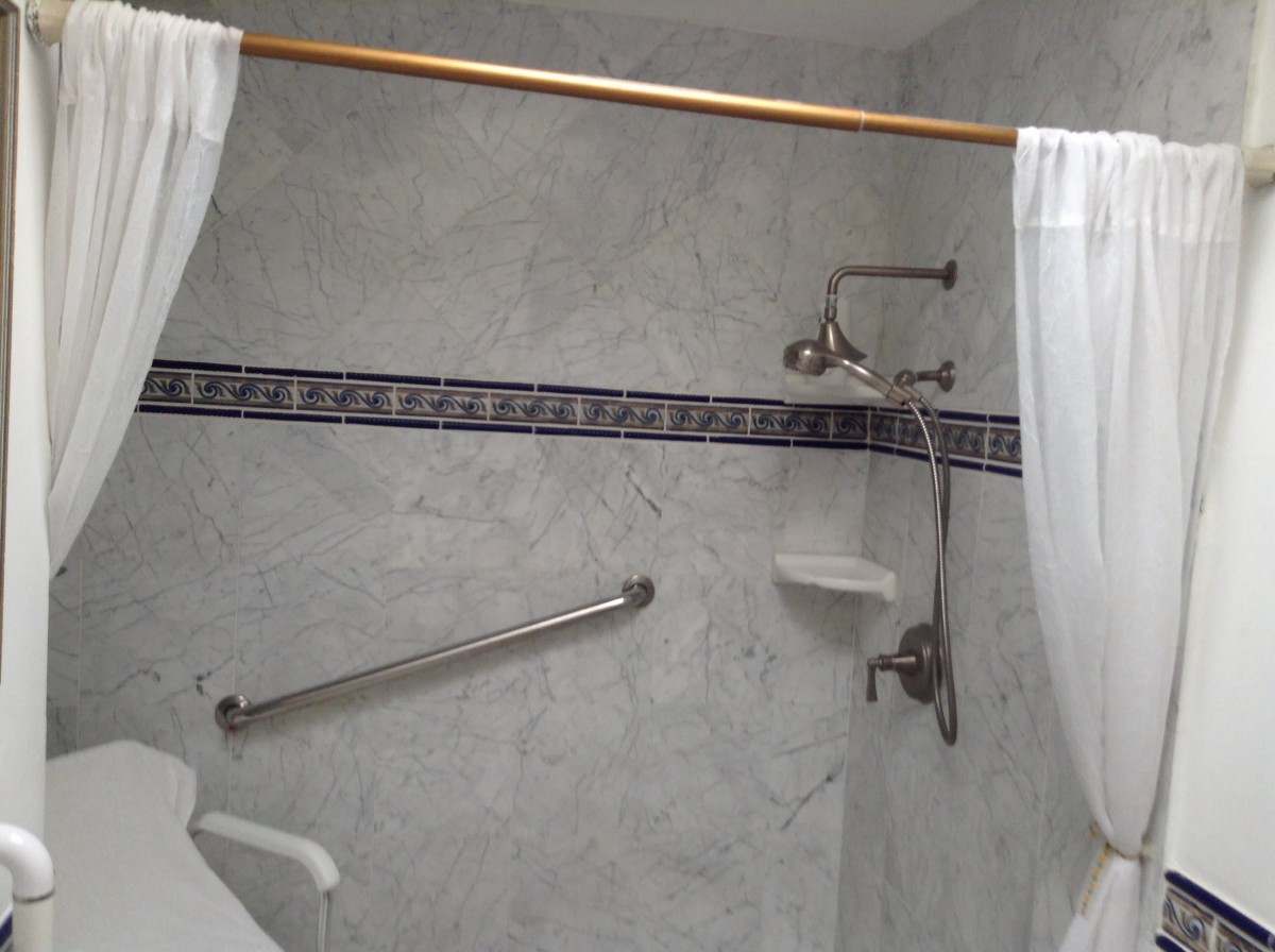 A bathroom shower area with a curtain, grab bar, and tiled wall featuring a decorative border.