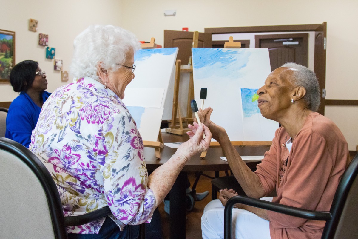 Two elderly individuals enjoying a painting session together in an art class.