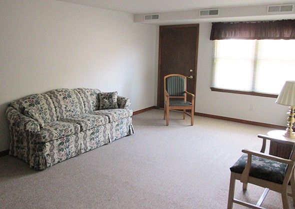 A minimalist living room with a patterned sofa, two chairs, and natural light from a window.