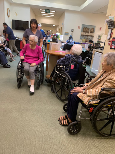 Residents in a care facility engage in a group setting with staff assistance.
