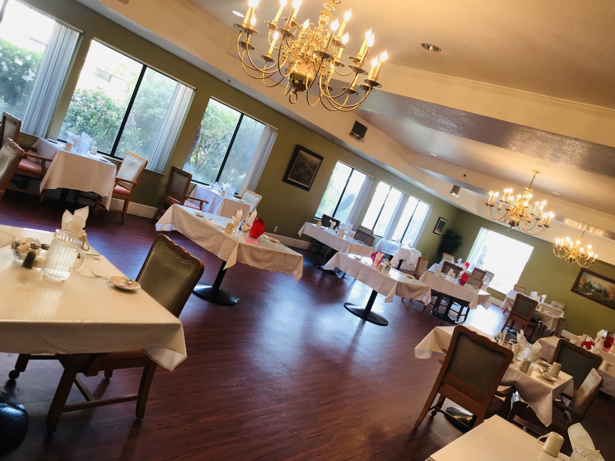 An elegant dining area with neatly arranged tables and chairs, illuminated by chandeliers.