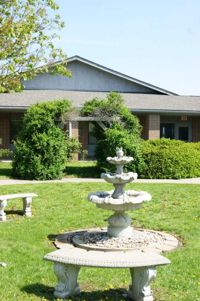 A garden with a fountain and bench in front of a building.