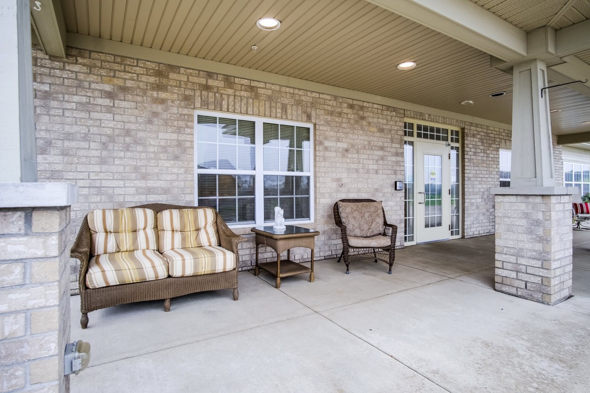 A cozy patio with outdoor furniture, featuring a sofa, armchair, and table against a brick wall.