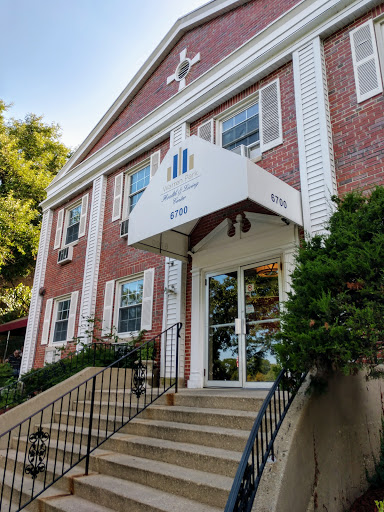 The entrance of a charming brick building featuring a canopy and landscaped surroundings.