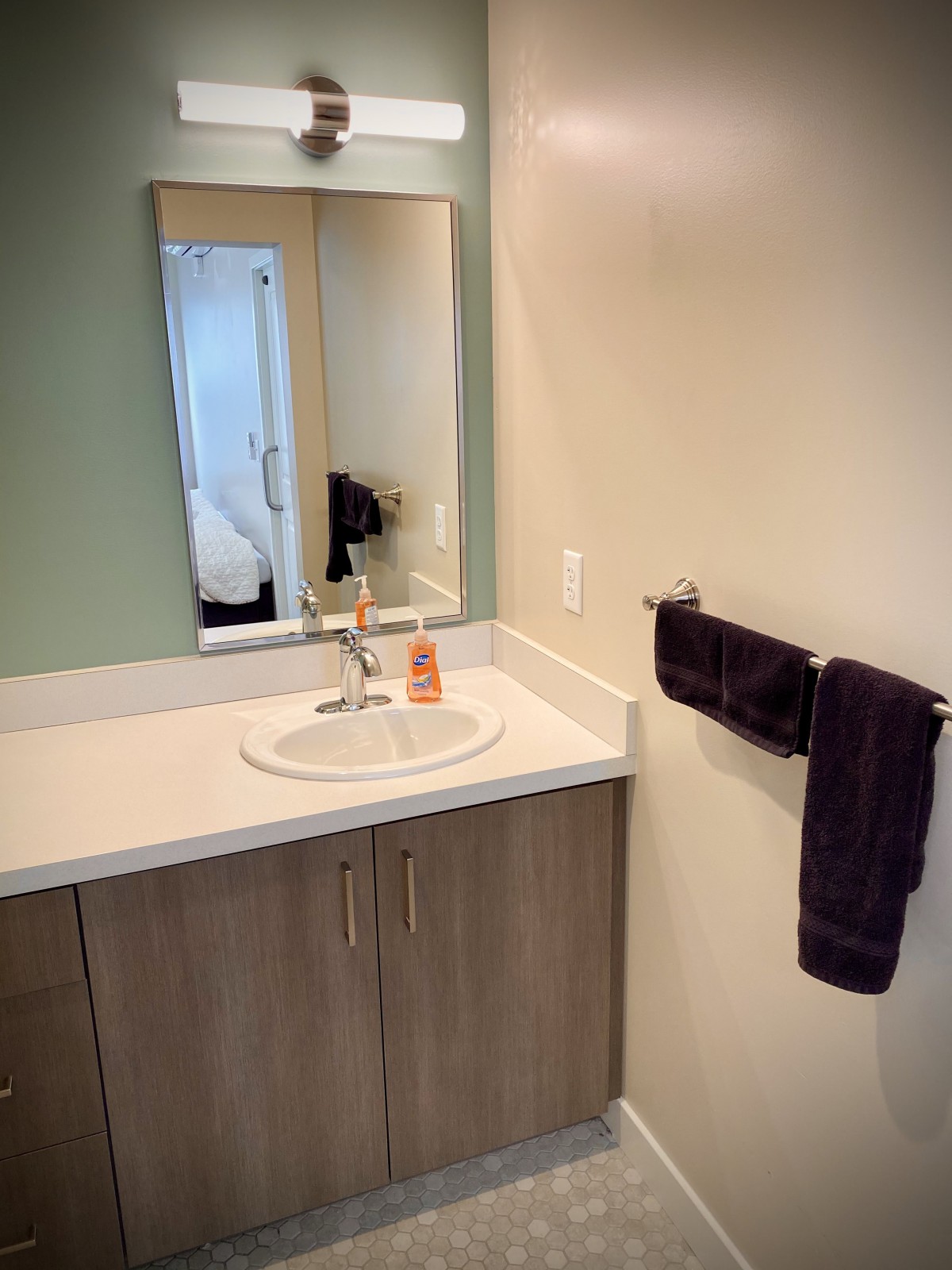 A minimalist bathroom featuring a sink with a mirror above, a set of towels on the wall, and a simple countertop.