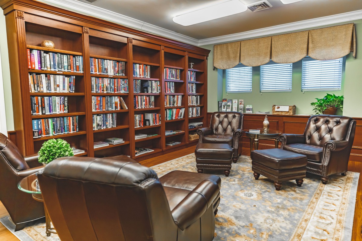 A cozy library with wooden bookshelves filled with books, comfortable leather armchairs, and a warm atmosphere.