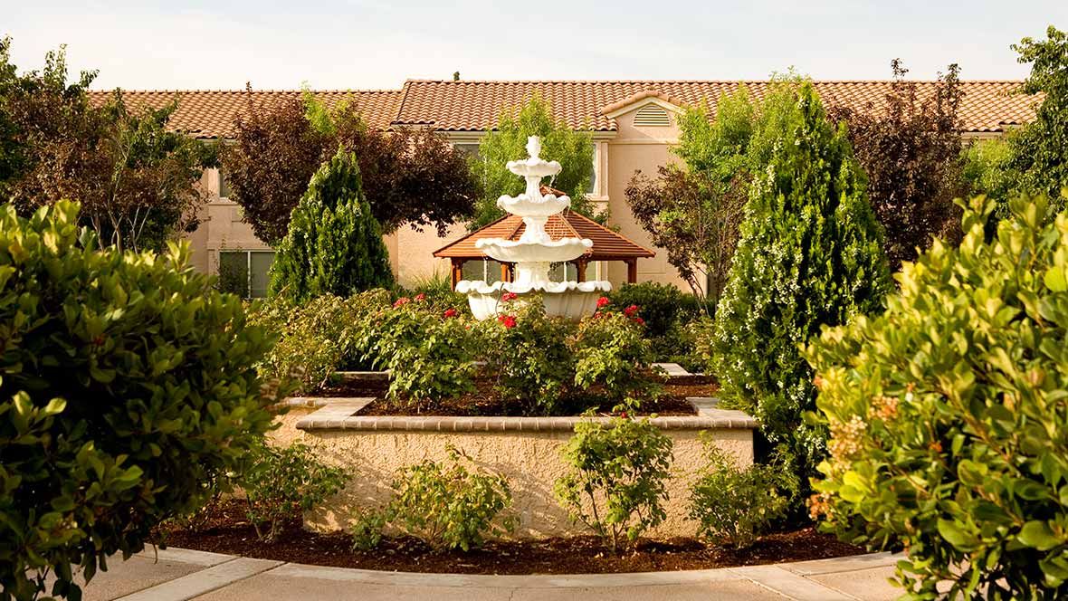 A beautifully landscaped garden featuring a white fountain surrounded by lush greenery and trees.