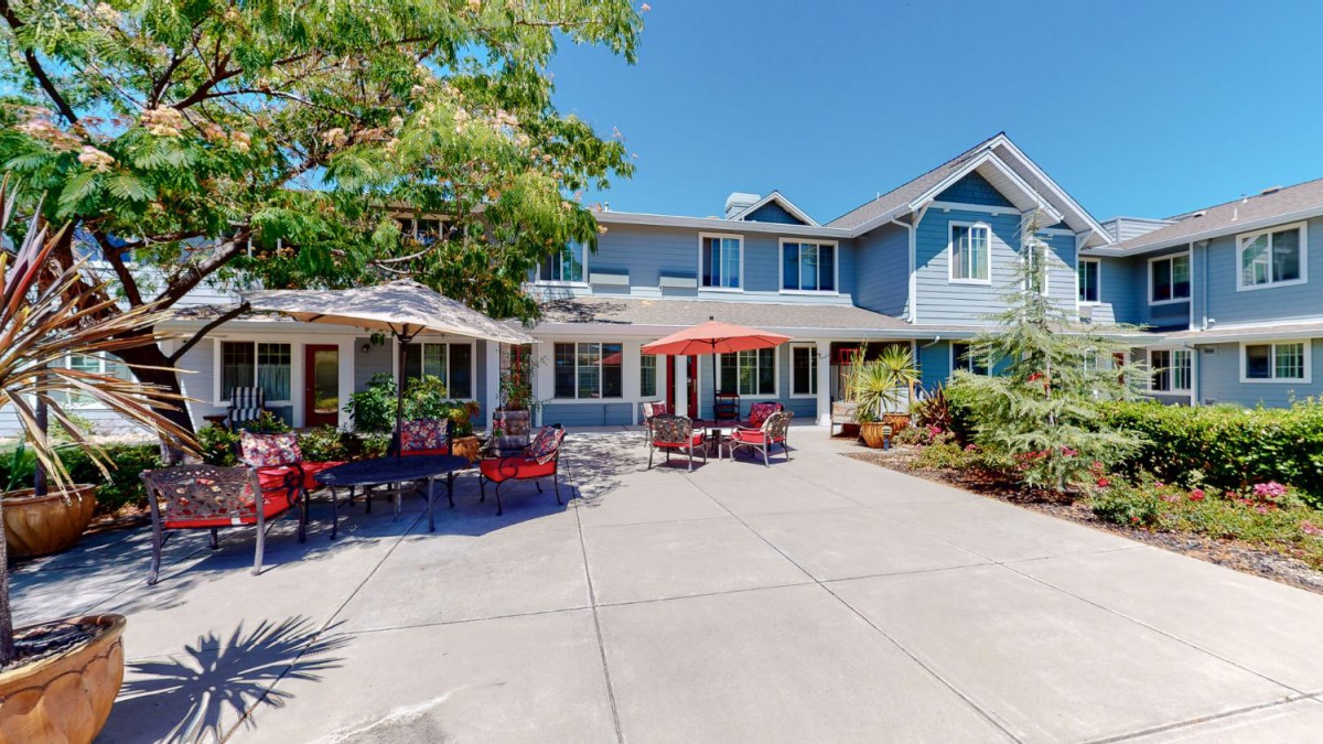 A spacious residential building with a welcoming patio area featuring outdoor seating and umbrellas on a sunny day.