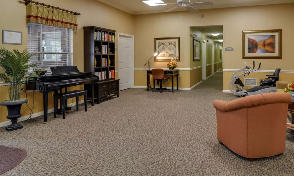 A cozy living area with a piano, bookshelf, desk, and sofa leading to a hallway.