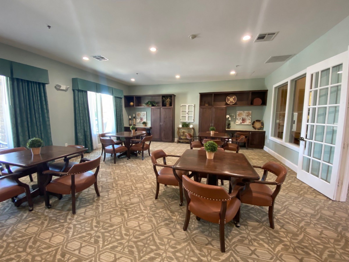 A cozy dining room with several tables and chairs, decorated with warm lighting and carpeted floors.