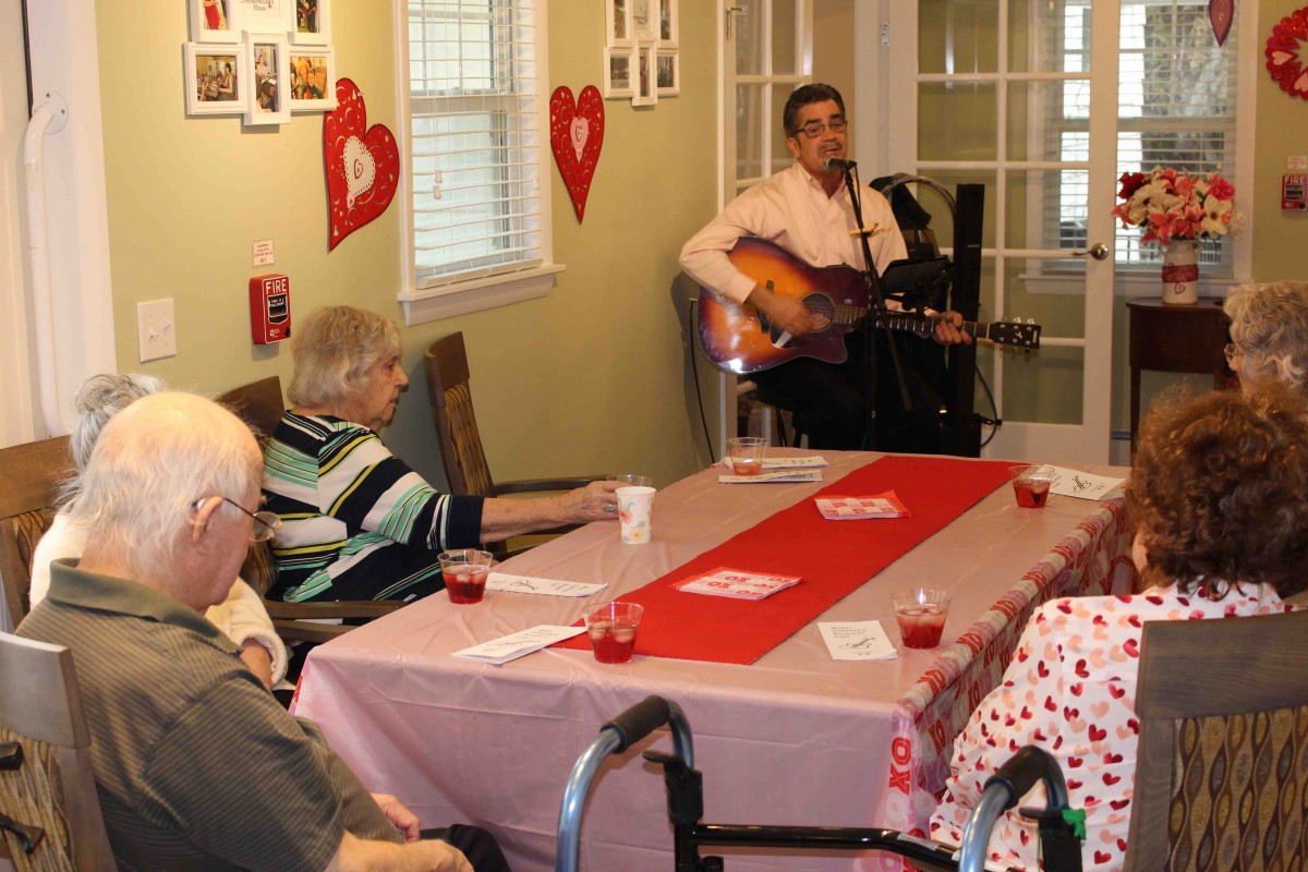 A musician performs for a group of elderly people in a room decorated with Valentine's Day hearts.