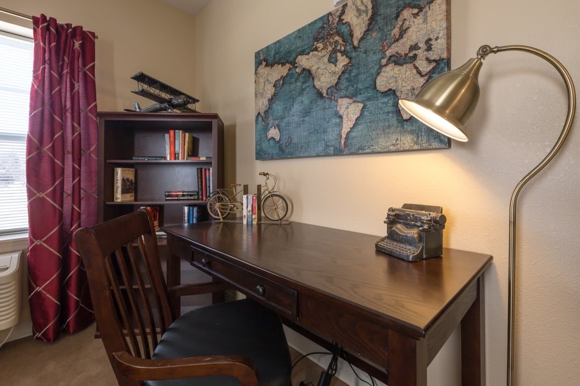 A cozy home office setup with a wooden desk, bookshelf, and a world map on the wall.