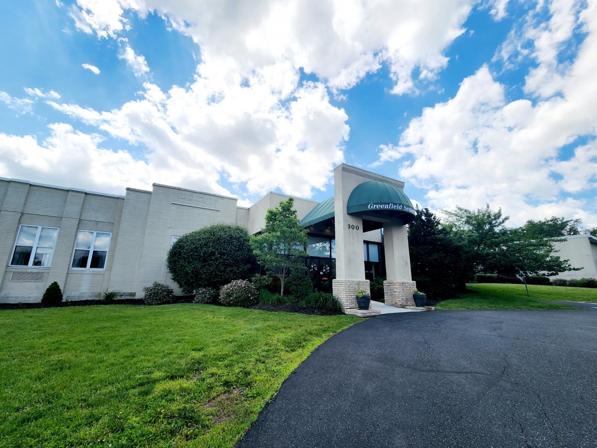 A building with an arched entrance and a driveway, set against a backdrop of a partly cloudy sky.