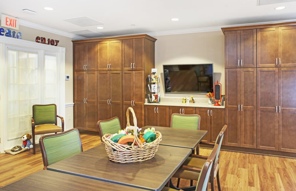 A spacious kitchen and dining area featuring wooden cabinets, a table with chairs, a basket of fruit, and a television.